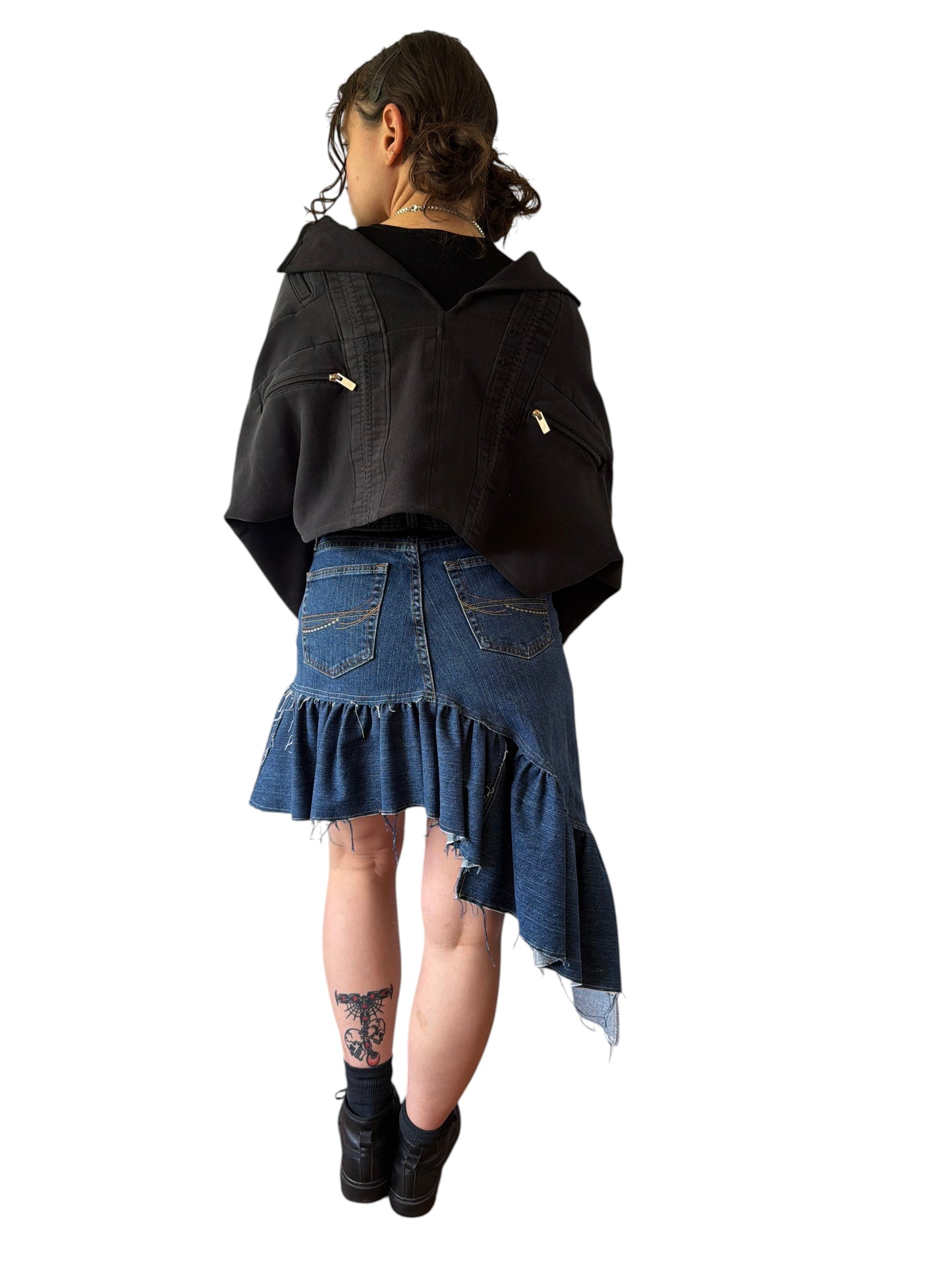Model wearing a 0 mph black upcycled shrug made from pants and flannel scraps, styled over a denim skirt.