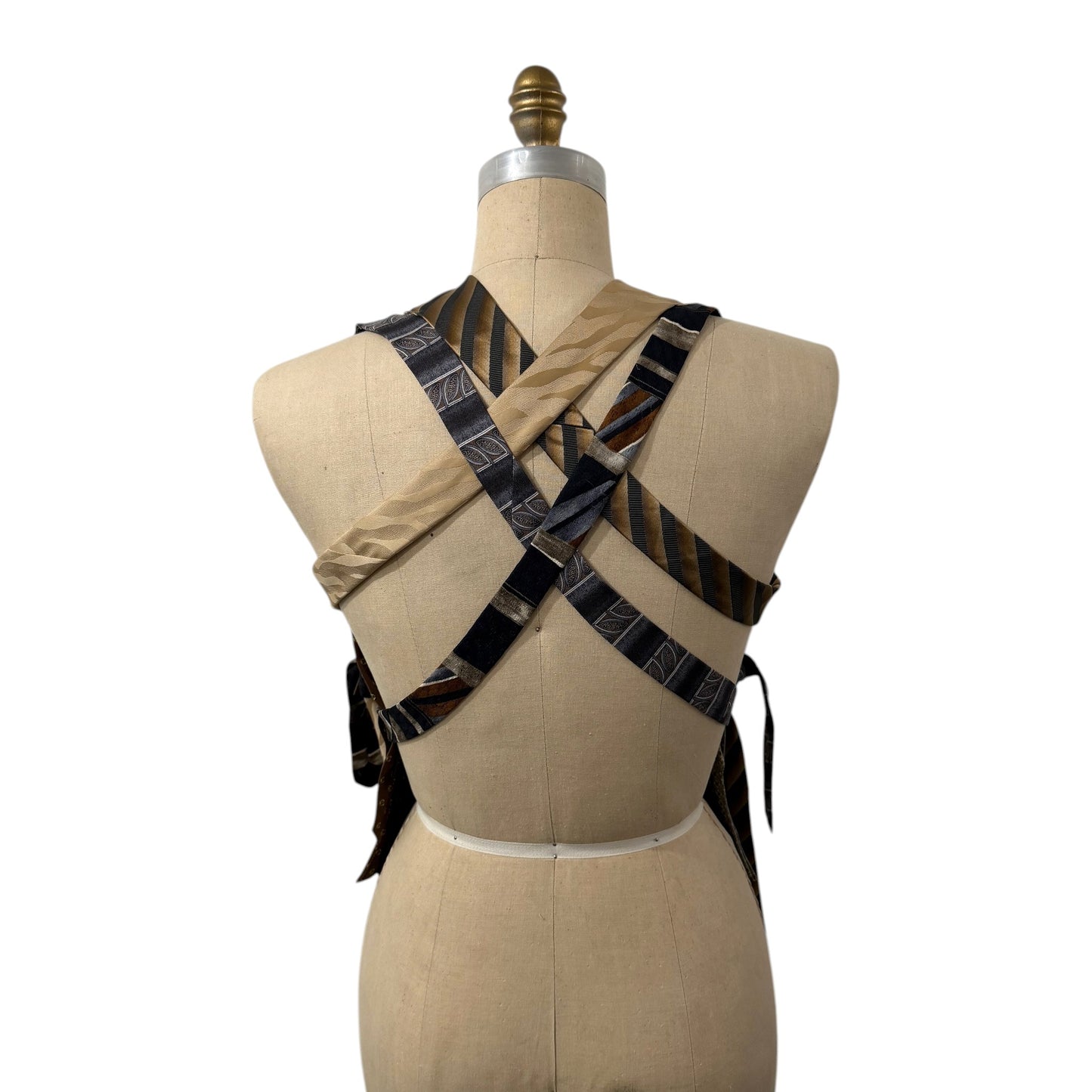 0 mph upcycled necktie patchwork vest in earthy tones with a crisscross back design on a dress form mannequin.