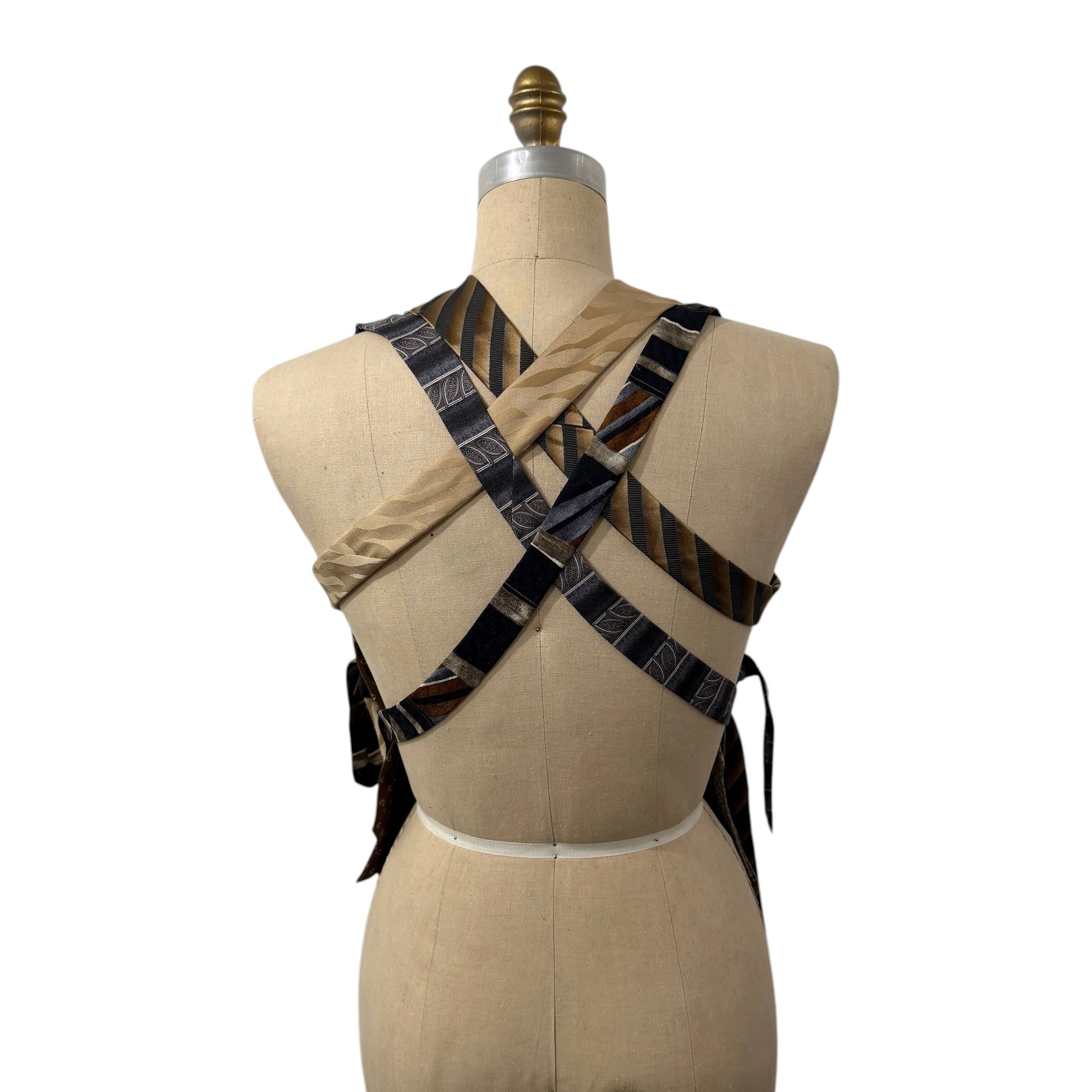 0 mph upcycled necktie patchwork vest in earthy tones with a crisscross back design on a dress form mannequin.