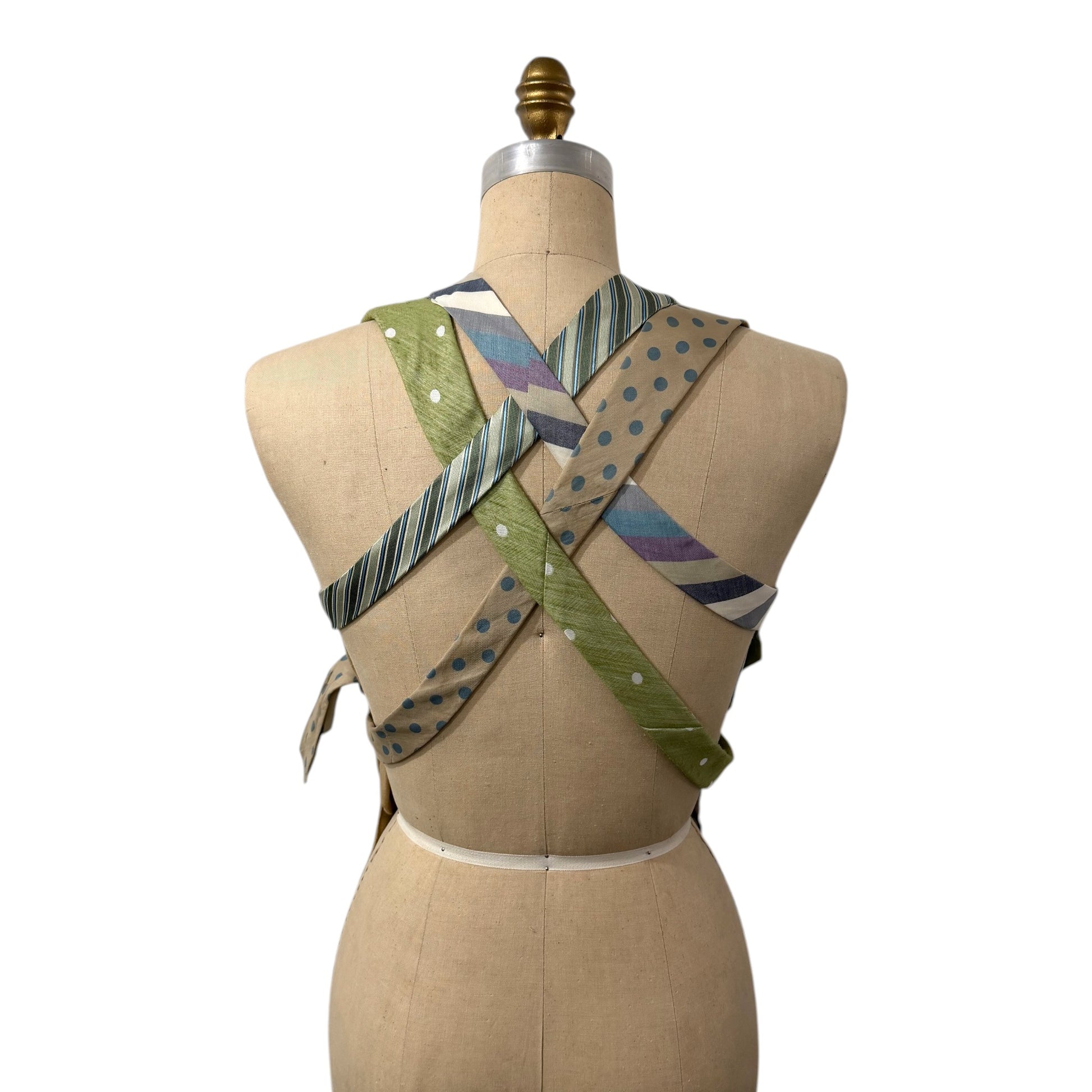 0 mph upcycled necktie vest with crisscross back straps in sage green, tan, and blue vintage patterns on a mannequin.